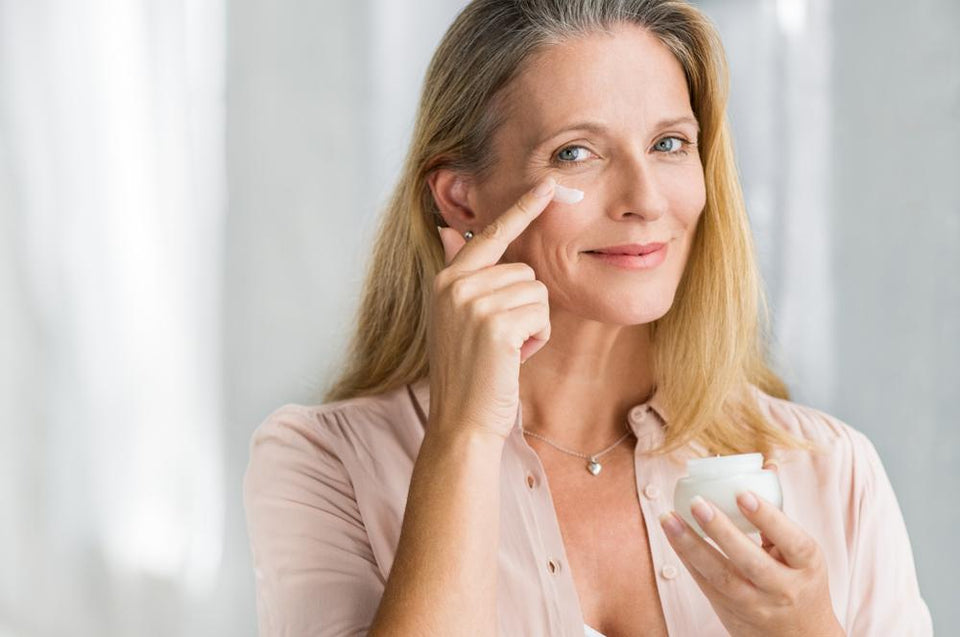 A happy woman applying cream under her eye.