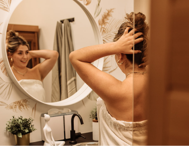 Woman smiles in mirror after visiting Flirt Cosmetics Studio Medical Spa